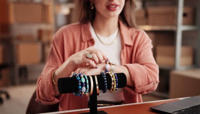 Pick a bracelet type that matches how you will wear it | tycoonstory media Woman showcasing multiple beaded and metal bracelets, including a stylish gold bracelet, while demonstrating jewelry on a display stand.
