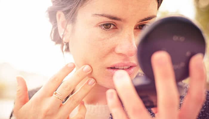 Understanding the regulation of cosmetics is important to winning product safety and personal injury cases in the cosmetic industry | tycoonstory media Woman examining facial skin concerns in a mirror, highlighting potential health risks in the cosmetic industry from unsafe cosmetic products and personal care services.