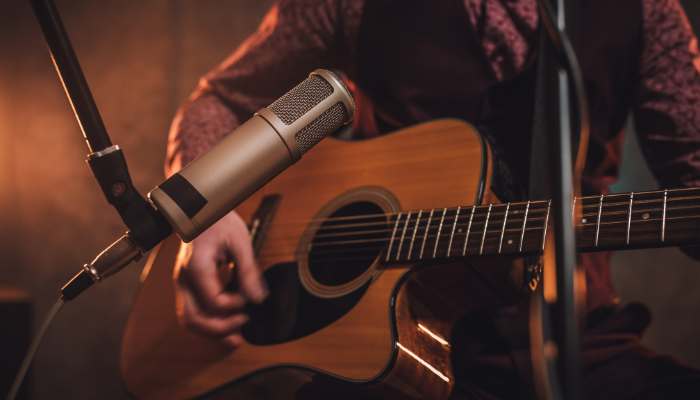 Guitar riffs defined 1 | tycoonstory media Close-up of a person playing an acoustic guitar with a microphone in a dim stage setting.