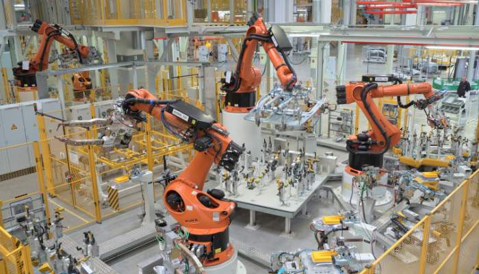 How ai autonomy software empowers industrial robotics 1 | tycoonstory media Industrial robotics on an automotive assembly line with multiple orange robotic arms assembling parts at a worktable in a factory.