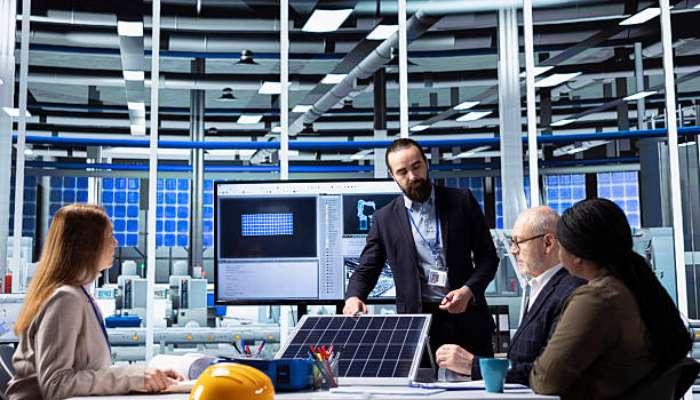 _how an energy adviser helps businesses cut power costs 1 | tycoonstory media Team in a high-tech lab discussing a solar panel project at a conference table with screens in the background.