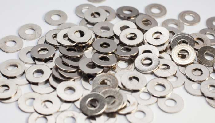 How custom washers solve fit and performance issues in assemblies 1 | tycoonstory media Pile of small metal washers scattered on a white surface, shiny and circular with central holes