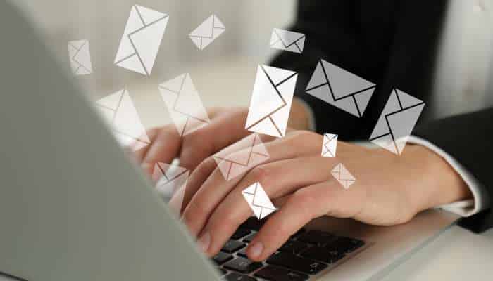 How kudositys bulk messaging platform helps businesses grow 1 | tycoonstory media Hands typing on a laptop with white email icons floating overhead, illustrating email communication in a business setting.