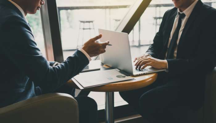 How large cap mf provides exposure to indias blue-chip equity universe 1 | tycoonstory media Two professionals in suits discuss at a small round table with an open laptop and documents nearby.