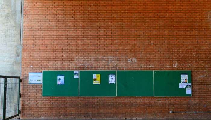 How large notice boards improve workplace communication 1 | tycoonstory media Brick wall with a long green bulletin board displaying posters and notices outside a building.