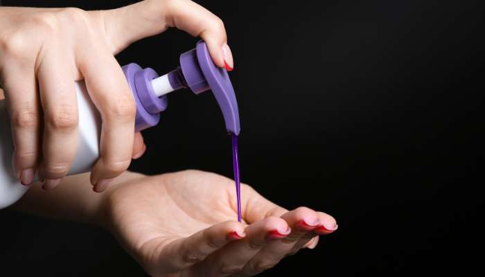 How toning products work against warm pigment and why timing changes everything | tycoonstory media Close-up of a hand pumping purple liquid from a bottle onto the other palm, likely nail polish or lotion, against a dark background.