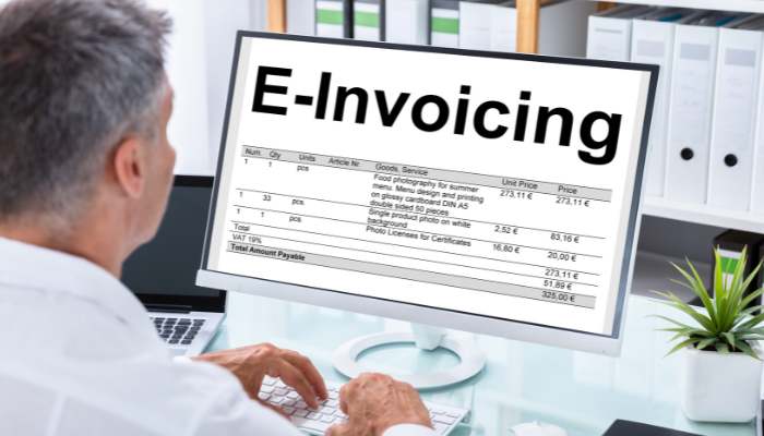 Is your business compliant with the spanish e-invoicing 1 | tycoonstory media Person at a desk viewing a monitor displaying the word 'e-invoicing' with an itemized invoice on screen.