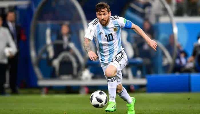 Messi 1 | tycoonstory media Argentine soccer player in number 11 jersey dribbles a ball on a green field, wearing bright green cleats and a captain's armband.