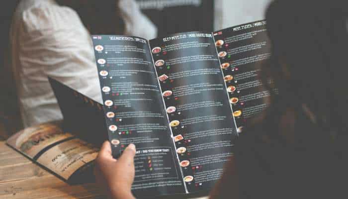 Nutritional transparency and hyper-personalized menus 1 | tycoonstory media Two people hold and read a large, multi-page restaurant menu at a wooden table.