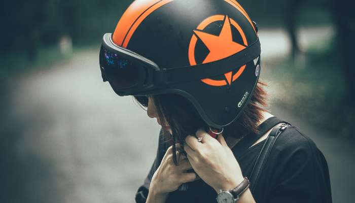 Open face helmet guide 1 | tycoonstory media Person in a black bike helmet with an orange star logo adjusting the chin strap.