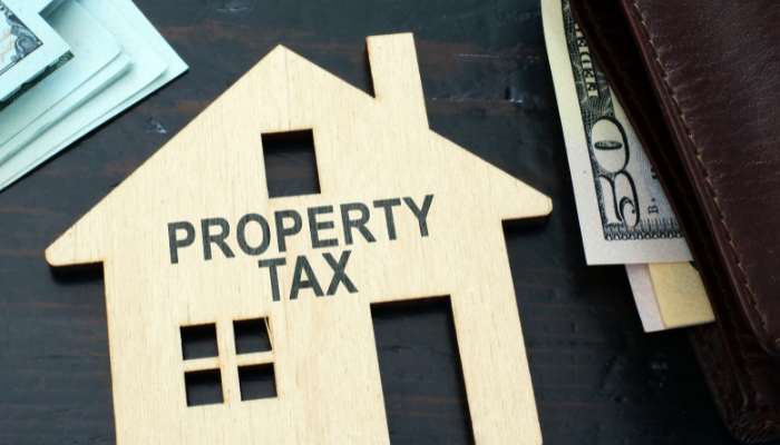 Property taxes and exemptions shape monthly costs | tycoonstory media Wooden house model with the words 'property tax' beside scattered cash and a wallet nearby.