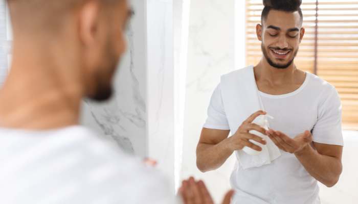 Protect your face with daily spf | tycoonstory media Smiling man in a white shirt dries his hands with a towel in a bright bathroom, seen in the mirror reflection