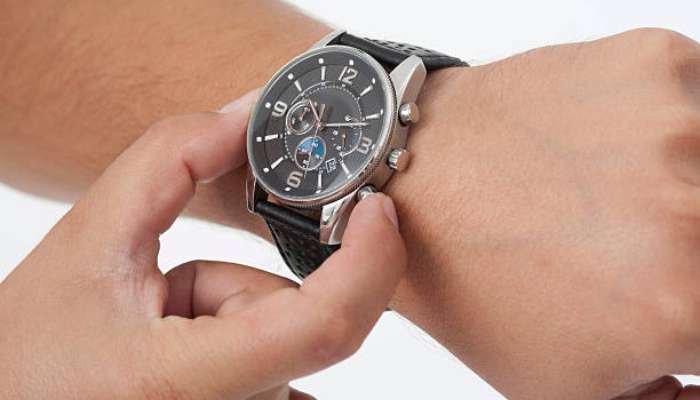 Scalp health 2 | tycoonstory media Person adjusting a black leather‑strapped wristwatch on their left wrist, showing the watch face with multiple dials and silver case.