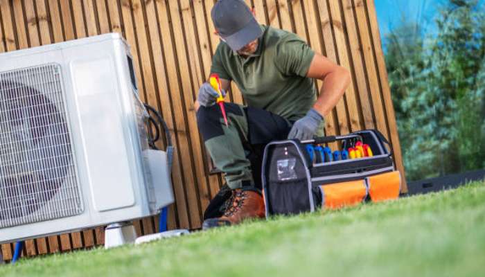 Signs your air conditioner is nearing the end of its service life 1 | tycoonstory media Hvac technician kneels on the grass, repairing an outdoor condenser unit with a toolkit nearby.