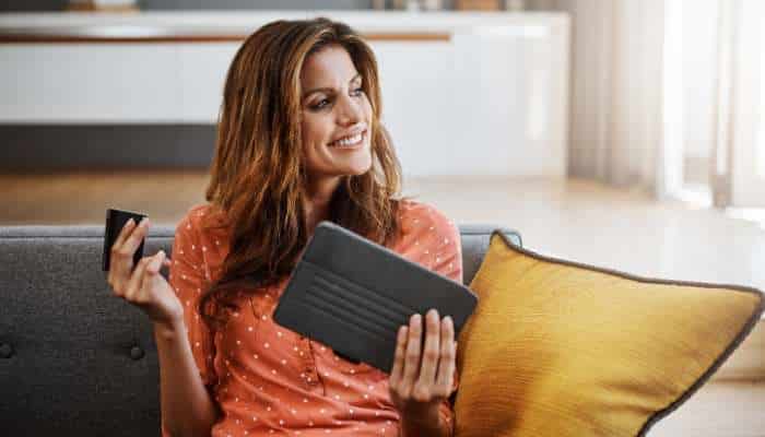 Smart spending decisions for lifes biggest purchases 1 | tycoonstory media Woman sitting on a sofa, smiling, holding a dark wallet and a smartphone marked as a shopping or payment moment.