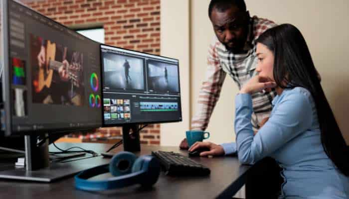 The real reason your startups videos look amateur 1 | tycoonstory media Two people collaborate at a desk with a multi-monitor setup showing video editing software and timelines by the monitors, with headphones on the desk.