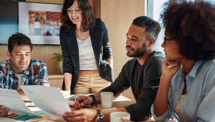 The reviews are in yeco is changing the game when it comes to finding your next agency 1 | tycoonstory media A group of four coworkers collaborates around a table with a laptop and papers, sharing ideas in a bright office.