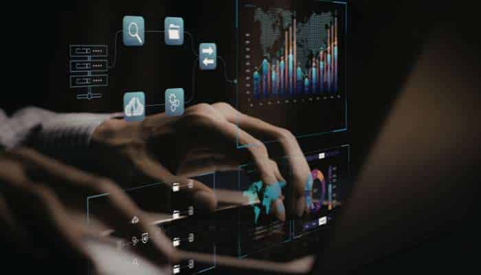 The tech-stack tax 1 | tycoonstory media Hands manipulating a futuristic transparent touchscreen with floating blue icons and data charts.