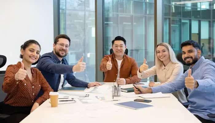 They reinforce a positive workplace culture - tycoonstory | tycoonstory media Five colleagues of diverse backgrounds seated at a conference table, smiling and giving thumbs up in a modern office setting.