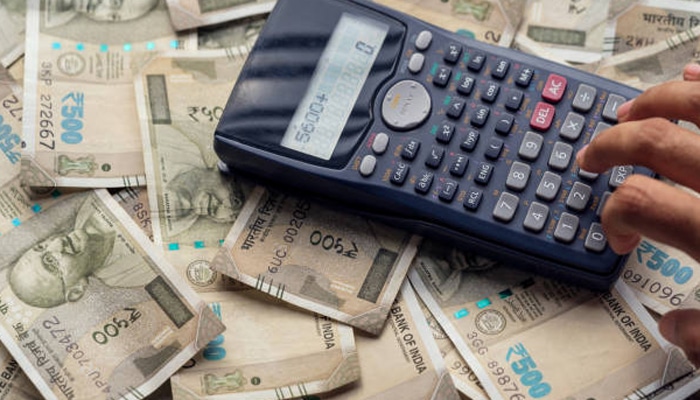 Untitled-1 | tycoonstory media Blue calculator on top of scattered indian ₹500 notes; a hand presses its keys.