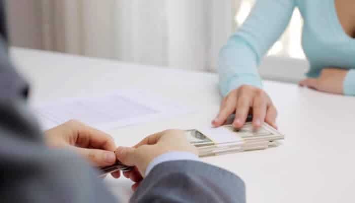 Short-term borrowing: when it may fit and how to compare safely | tycoonstory media Person receiving cash during a short-term loan discussion, illustrating emergency expense options and the importance of comparing borrowing costs and repayment terms safely.
