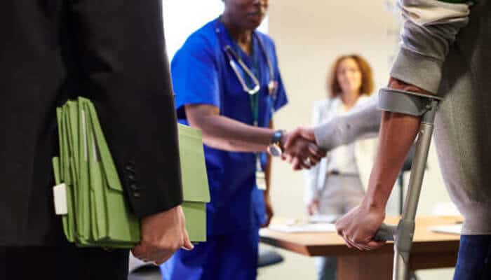 Understanding car accident injury claims | tycoonstory media Injured car accident patient using a crutch while meeting medical and legal professionals about injury claims and possible medical malpractice concerns.