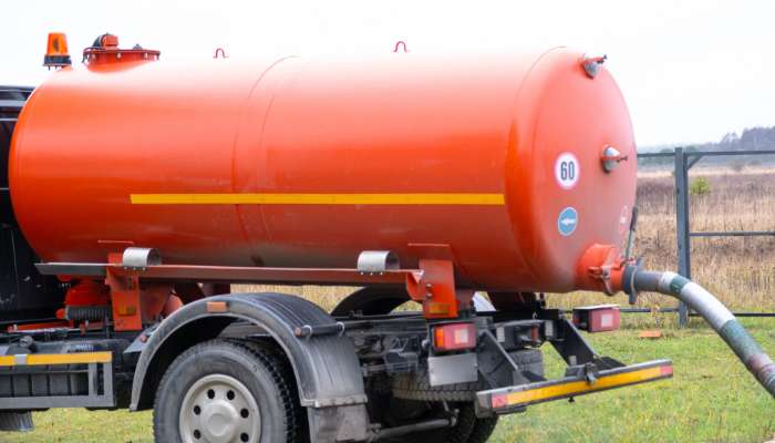 Warning signs your system needs immediate attention 1 | tycoonstory media Orange cylindrical tanker trailer attached to a truck, with a hose connected to the rear in an open field.