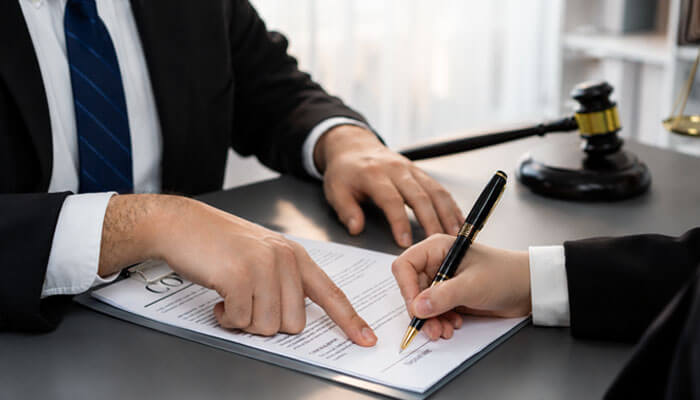 We ran the full document and read the disagreements - tycoonstory | tycoonstory media Two professionals sign a legal document at a desk, one pointing to the page while the other writes with a pen, with a gavel nearby on the table.