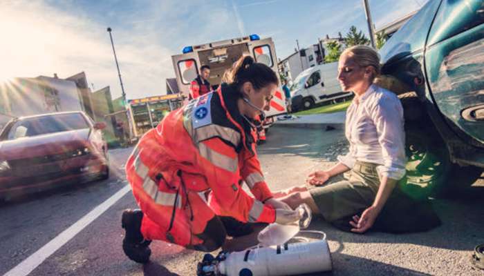 What accident victims should know about personal injury claims in texas 1 | tycoonstory media Paramedic kneels beside a woman on a road after a car crash, checking her vitals with an oxygen tank nearby.