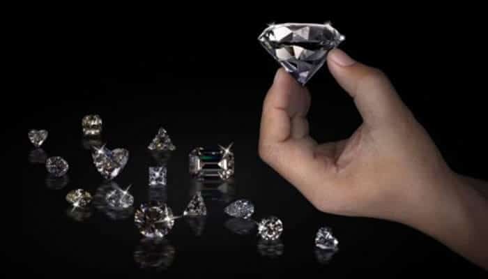 What drives price in plain english - tycoonstory | tycoonstory media Hand holding a large cut diamond above a collection of loose diamonds on a black background.
