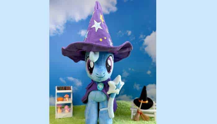 What makes symbiote studios trixie lulamoon deluxe plush stand out from standard plush toys 2 | tycoonstory media Trixie lulamoon deluxe plush wizard pony with star cape standing in fantasy outdoor set with props and sky backdrop