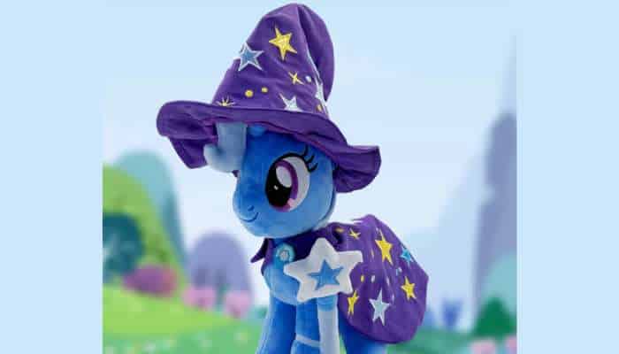 What makes symbiote studios trixie lulamoon deluxe plush stand out from standard plush toys 3 | tycoonstory media Trixie lulamoon deluxe plush close-up portrait wearing purple wizard hat and star cape against soft fantasy landscape