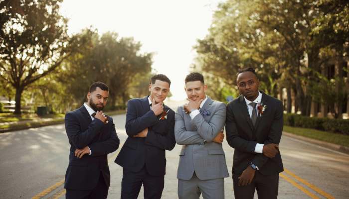 Why bespoke mens suits are a staple for formal occasions 1 | tycoonstory media Four men in suits posing on a sunny street, arms folded, looking confident in a casual group photo.