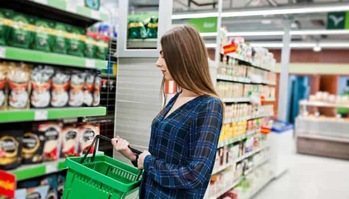 Why hanshow is a strategic esl partner - tycoonstory | tycoonstory media Woman in a blue plaid shirt examines groceries on a store shelf while pushing a green shopping basket.