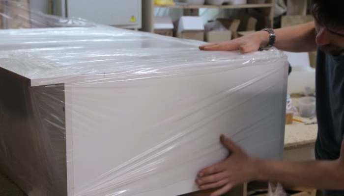Why polypropylene sheet is a preferred material for sustainable packaging 1 | tycoonstory media Person wrapping a large appliance in plastic for shipping in a workshop.