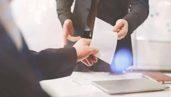 Answer engines and the future of how clients find law firms 1 | tycoonstory media Two businesspeople exchange a document across a desk in a bright office setting, with a laptop visible nearby.