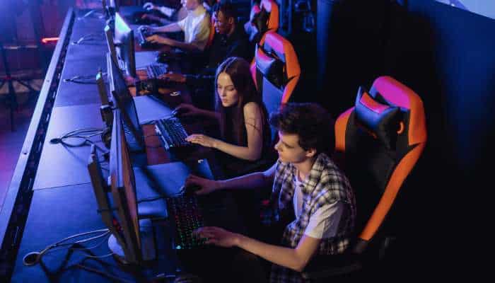 Beyond better graphics 1 | tycoonstory media Group of young gamers at a lan party playing on desktop computers in a dimly lit arena with neon lighting.