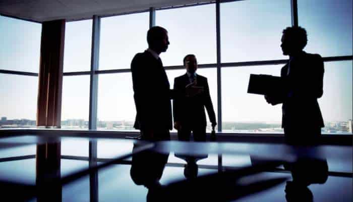 Can governments keep up with online gambling 1 | tycoonstory media Silhouetted professionals in a modern office discuss by a large window, city skyline visible outside.