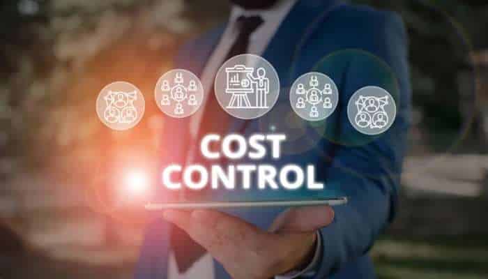 Cost control | tycoonstory media Businessperson in a blue suit holding a tablet that shows the words cost control with circular icons above the screen.