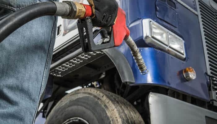 Dbhynj 1fuel efficiency keeps climbing the priority list - tycoonstory | tycoonstory media Person fueling a blue heavy-duty truck with a diesel nozzle, close-up on the nozzle and tire.