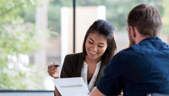 Does your business need a loan for growth working capital or asset purchase 1 | tycoonstory media Smiling woman in a blazer shows a document to a man across a table in a bright office.