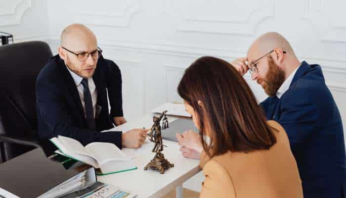 Drug charges in georgia 1 | tycoonstory media Three professionals in suits sit around a white desk in a bright office, reviewing documents, with a small statue of lady justice on the table.