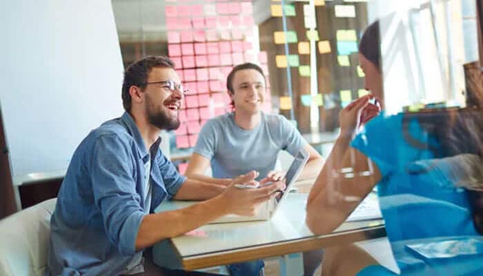 Essential tools for online business ideas - tycoonstory | tycoonstory media Team members brainstorm at a glass table with laptops as colorful sticky notes cover the wall behind them.