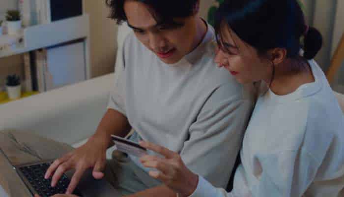 Forex card vs credit card 1 | tycoonstory media Two people sit close together, looking at a laptop with a credit card in hand, suggesting online shopping.