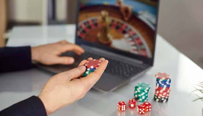 Free spins vs bonus credits at mrgroup88 free credit casino a beginners comparison 1 | tycoonstory media Person holds red poker chips in front of a laptop displaying a roulette wheel game