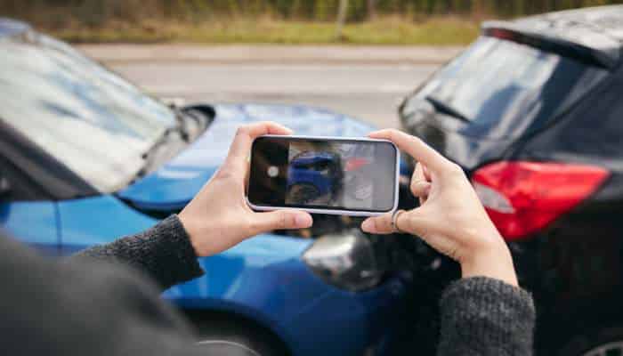 How a car accident attorney can help with insurance claims 1 | tycoonstory media Person holds a smartphone to photograph a blue car damaged in a rear-end collision between two vehicles.
