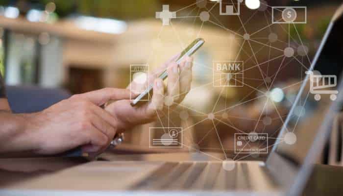 How open banking is improving payment security and fraud prevention 1 | tycoonstory media Hands using a smartphone with floating finance icons (bank, credit card, wallet) and a connected network, illustrating mobile banking and digital payments.