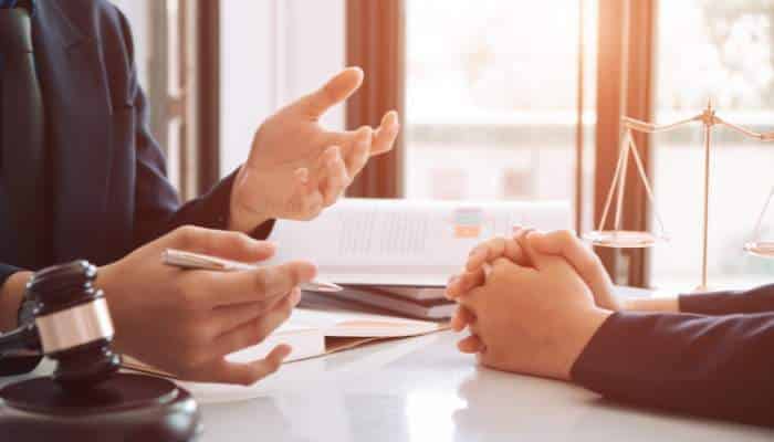 Injured in bergen county 1 | tycoonstory media Lawyer gesturing while discussing documents with a client at a desk; a gavel and scales of justice are visible on the table.