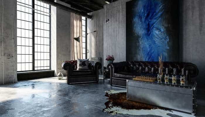 Is polished concrete worth it for homes 1 | tycoonstory media Industrial loft living room with two black leather sofas, blue abstract painting, and a metal coffee table with whiskey glasses on a cowhide rug.