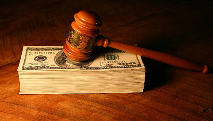 Powerfull actions | tycoonstory media Powerful interests influencing legal decisions with a judge’s gavel resting on money in a courtroom setting